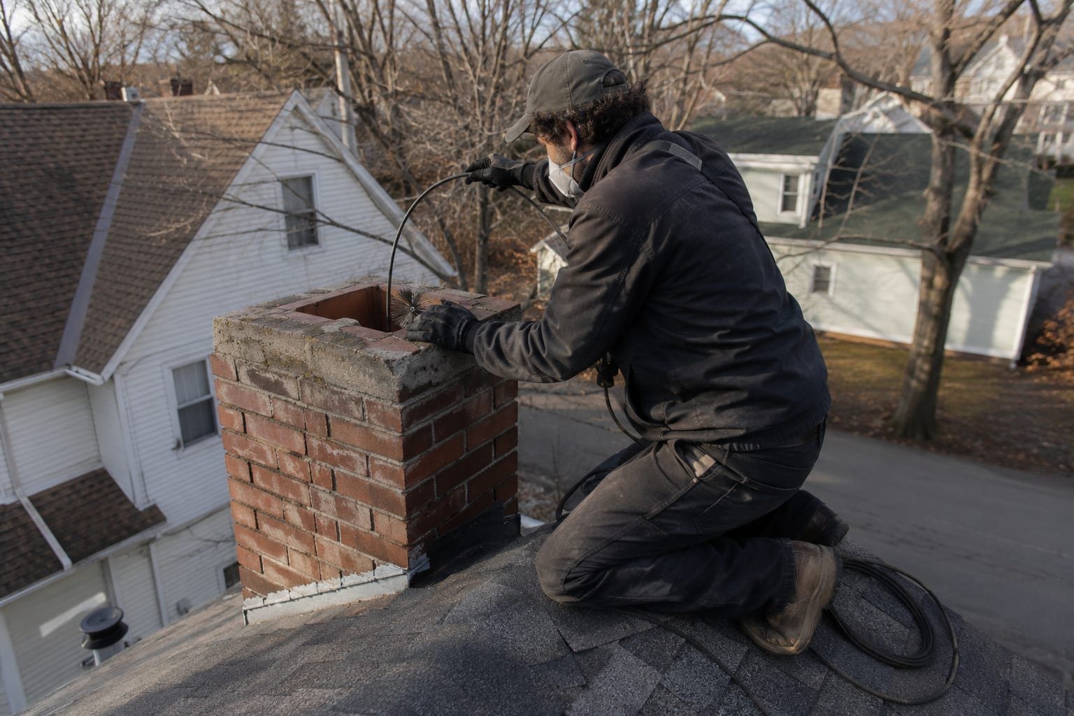 Chimney sweep working on a brick chimney above the roofline of a Syracuse, NY home