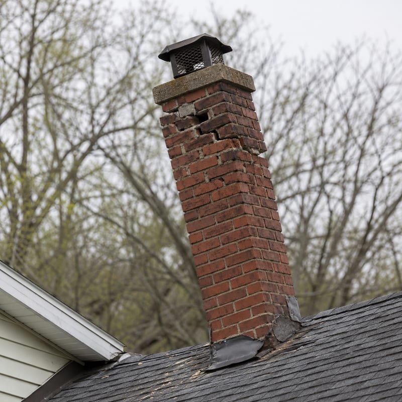 Leaning chimney stack with spalled brick above the roofline in Syracuse, NY