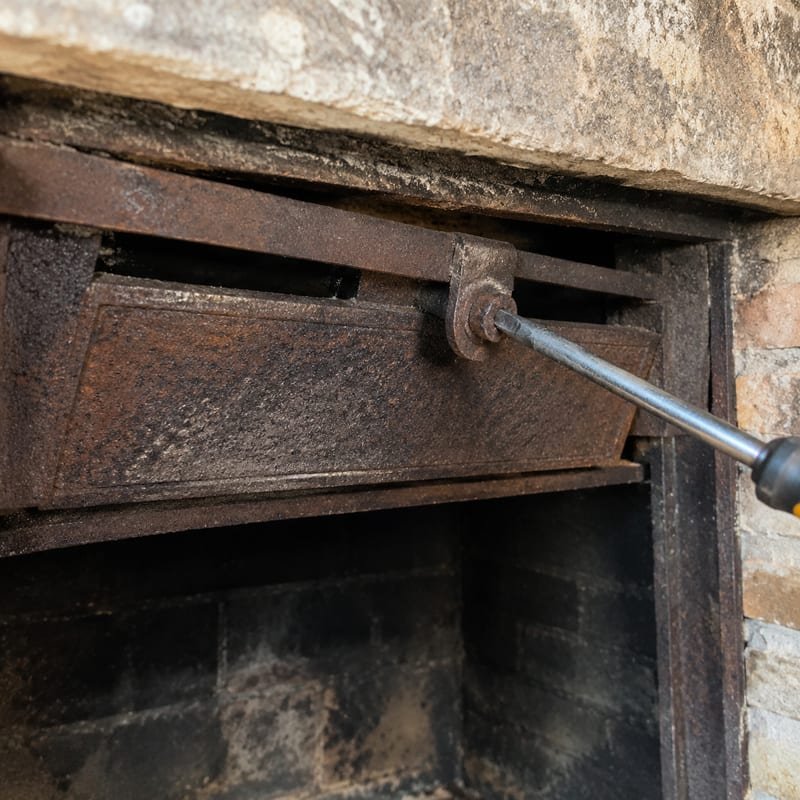 A rusted throat damper being replaced at the base of a masonry fireplace flue in Syracuse, NY